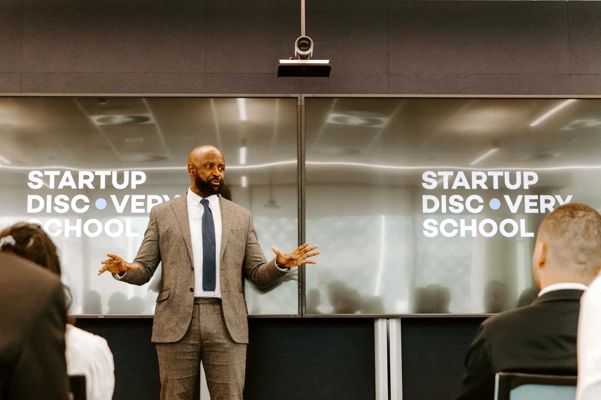 A speaker in a tweed suit addressing founders at Startup Discovery School