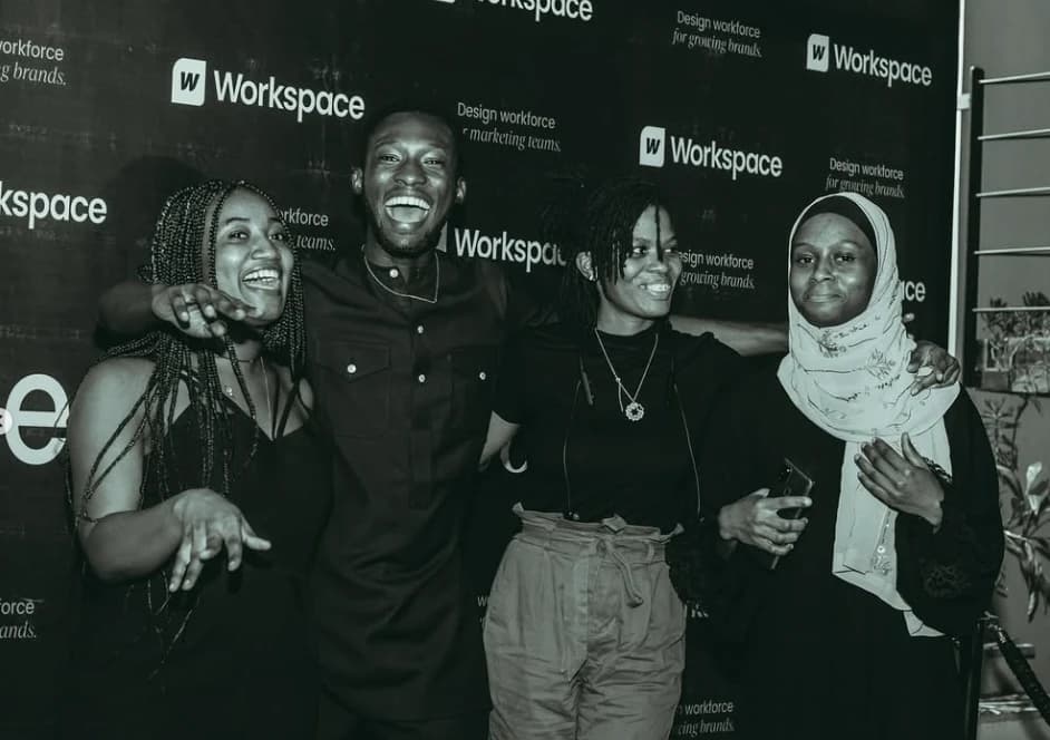 Four people laughing in front of the Workspace backdrop, in black and white