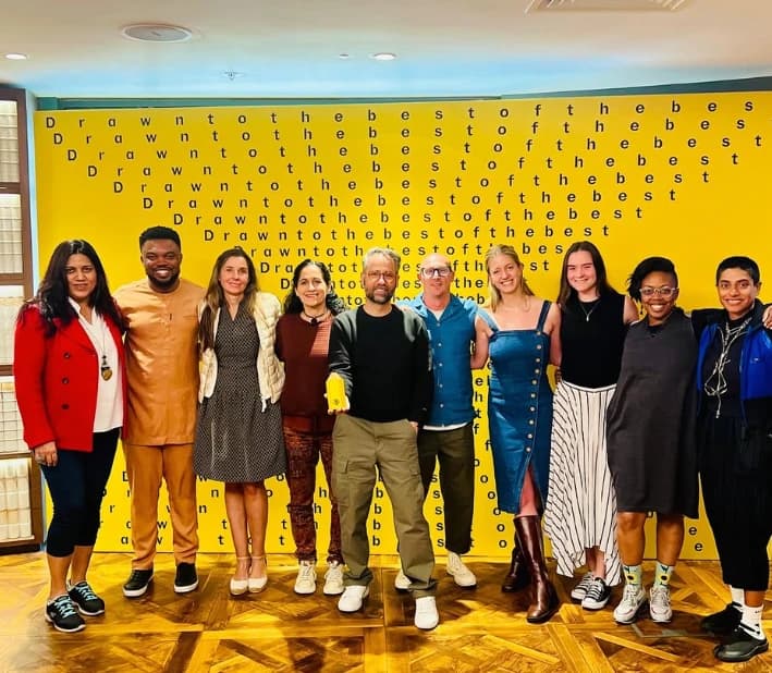 A group standing in front of a yellow wall of repeated lettering