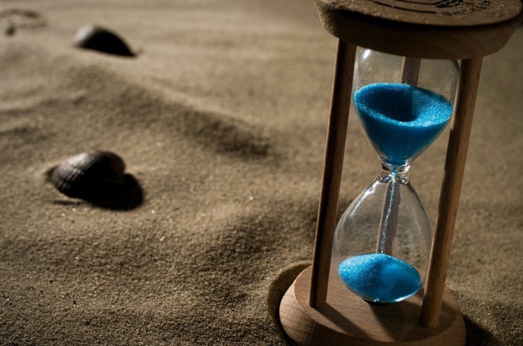 An hourglass with electric blue sand on a beach