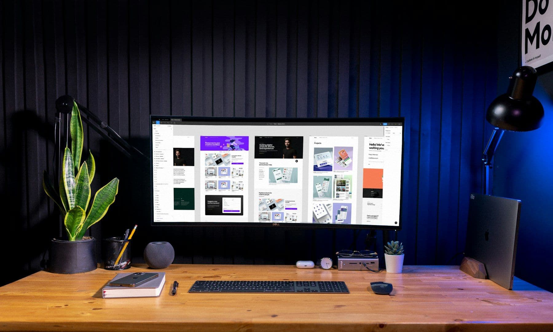 A designer's desk in a blue-lit studio, with brand layouts on a wide monitor